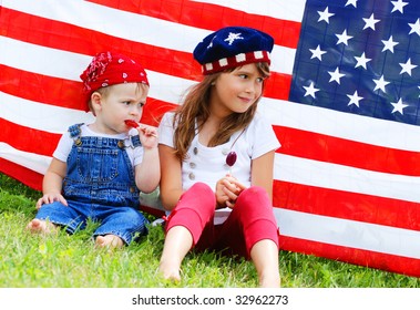 Two children sitting next to an american flag eating suckers