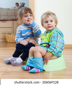 Two children sitting on bedpans in home interior