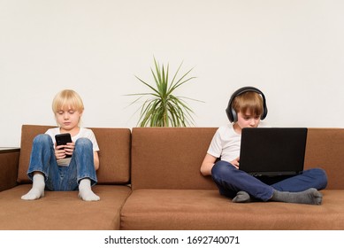 Two Children Sitting On Couch With Gadgets Smartphone And Laptop. Generation Alpha.