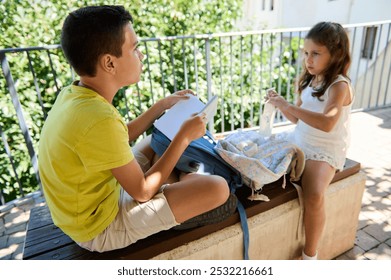 Two children sitting outdoors on a sunny day, sharing snacks and studying together, embodying friendship and learning. - Powered by Shutterstock