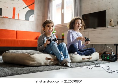 Two children small caucasian brother and sister happy children siblings boy and girl playing video game console using joystick or controller while sitting at home real people family leisure concept - Powered by Shutterstock