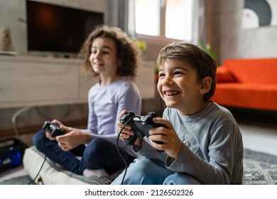 Two Children Small Caucasian Brother And Sister Happy Children Siblings Boy And Girl Playing Video Game Console Using Joystick Or Controller While Sitting At Home Real People Family Leisure Concept