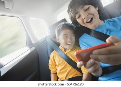 Two Children Travelling In The Back Seat Of A Car Sharing A Handheld Games Tablet,