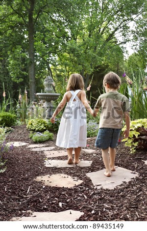 Two children walking down a garden path to a fountain
