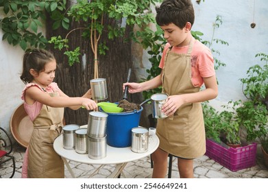 Two children wearing aprons engage in gardening using recycled tin cans and soil. The outdoor scene shows teamwork and sustainability in a cozy home garden setting. - Powered by Shutterstock