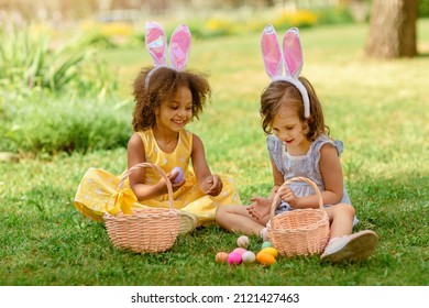 Two children wearing Bunny ears find and pick up multicolored egg on Easter egg hunt in garden