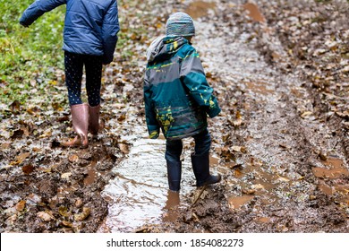 Two children wearing wellies walking through deep mud.