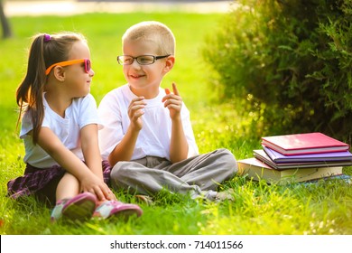 Two children of younger school age, the boy and the girl are reading books on the green grass. Warm spring day. School students have an excellent mood.