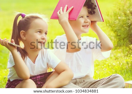 Two children of younger school age, the boy and the girl are reading books on the green grass. Back to school. Young student doing homework. Education for small kids.