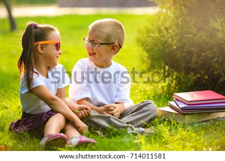 Two children of younger school age, the boy and the girl are reading books on the green grass. Warm spring day. School students have an excellent mood.