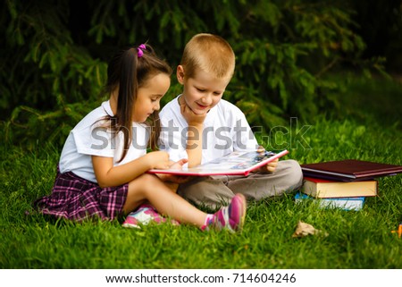 Two children of younger school age, the boy and the girl are reading books on the green grass. Back to school. Young student doing homework. Education for small kids.