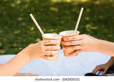 Two children's hands are holding eco-friendly cups and tubes with apple juice at a picnic in the park. Eco-friendly disposable tableware - Powered by Shutterstock