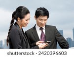 Two Chinese business people standing looking at smart mobile phone. Urban cityskyline in background.