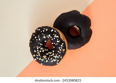 two Chocolate covered donuts with crush nuts on top. zenithal angle on colored background - Powered by Shutterstock