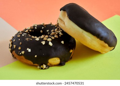 two Chocolate covered donuts with crush nuts on top on colored background - Powered by Shutterstock