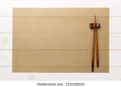 Two chopsticks and bamboo mat on wooden background. Top view, copy space.