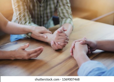 Two Christian people are praying for young man friends on wood table at church prayer room to encourage and support him in his problem and spiritual growth, small prayer group and fellowship concept