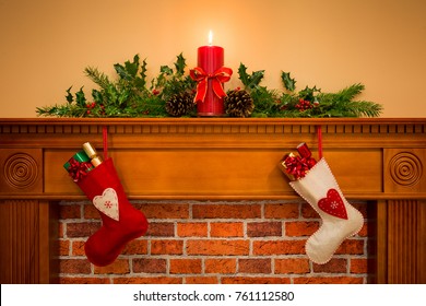 Two Christmas stockings with gift wrapped presents hanging on a mantelpiece over a fireplace, plus burning candle with festive garland including holly, fir and pine cones.