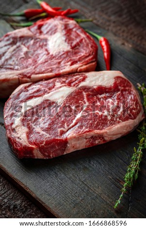 Two classic raw rib eye steaks with red hot peppers on a wooden Board