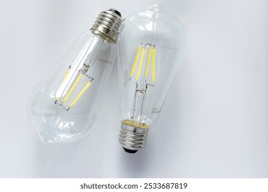 Two clear glass LED light bulbs with visible filaments are lying on a white background. - Powered by Shutterstock