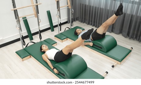 Two clients practicing leg raises using arc barrel equipment during a Pilates session. Group of happy trainer pose scissor or leg stretch pose for improving core muscle and lower abdominal. Habituate. - Powered by Shutterstock