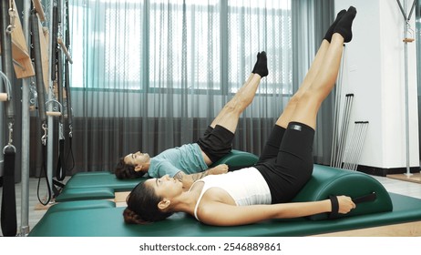 Two clients practicing leg raises using arc barrel equipment during a Pilates session. Group of happy trainer pose scissor or leg stretch pose for improving core muscle and lower abdominal. Habituate. - Powered by Shutterstock