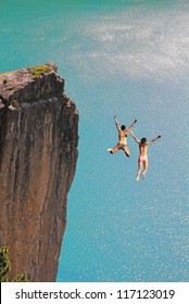 two cliff jumping girls, against turquoise ocean