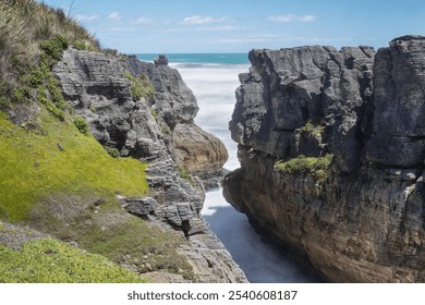 Two cliffs with a gap in-between with sea water rushing in.