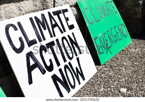 Two \'Climate action now\'\
and \'climate emergency\' signs rest on a sidewalk during a climate\
change march in London, Ontario, Canada in September, 2021. No\
people.