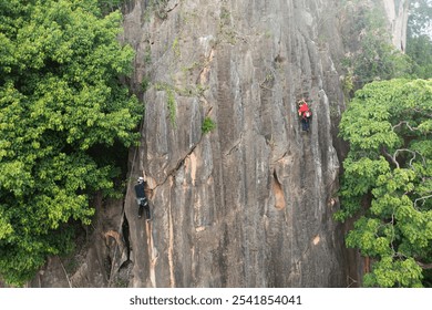 Two climbers scaling a vertical rock face flanked by dense green foliage.
 - Powered by Shutterstock