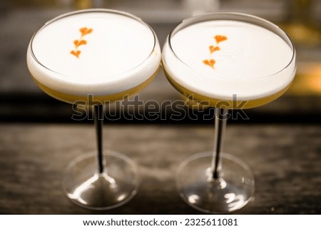 
two cocktail glasses with whiskey sour and heart-shaped angostura bitter drops in white foam