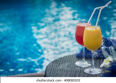 Two Cocktails Red And Yellow On Table Against Blue Swimming Pool. Travel, Luxury, Vacation Background. Detox Healthy Drink. Text Space