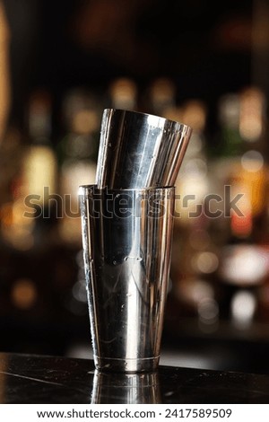 Two cocktails shaker glasses standing above each other on a bar desk. Cocktails and drinking in a pub. Cocktail shake stainless steel metallic glass.