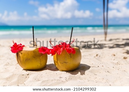 Two coconut cocktails on white sand beach next to clean sea blue water. Vacation and travel concept