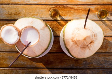 Two coconut milkshakes served in coconuts. One opened, one closed. With shot of rum, overhead top view