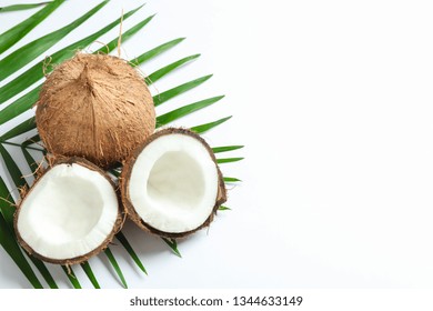 Two coconut one of which split with palm branch on white background