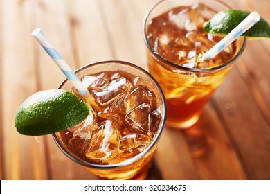 two cold glasses of iced tea with retro paper straw lime wedges on wooden table top. Shot with selective focus.