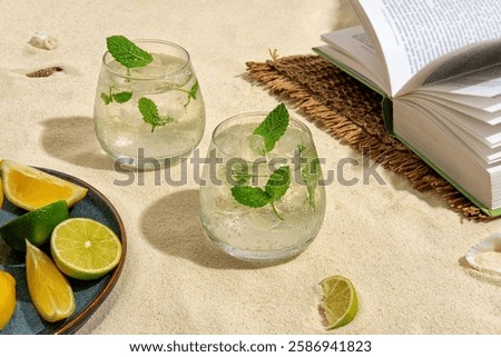 Two cold and refreshing cocktail with ice garnished mint standing on the sand, on the beach by the sea. Summer mint non-alcoholic cocktail with juice and soda. Hard light, bar menu.