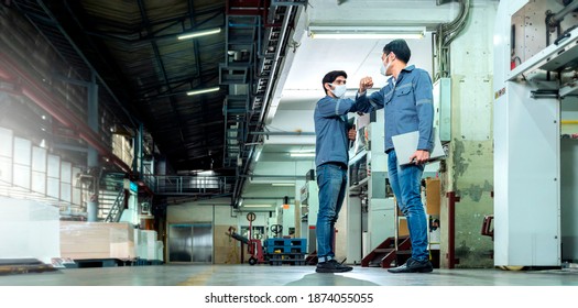 Two Colleague Engineer Workers In Warehouse Factory Wearing Facemask Have A Greeting Hello By Hit The Elbow Or Elbow Bump To Prevent The COVID Infection. New Normal Working Lifestyle Concept