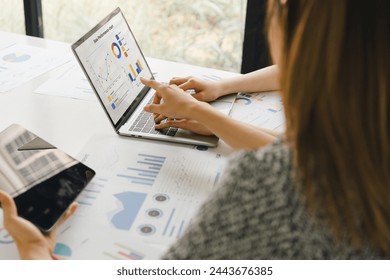 Two colleagues analyzing financial data reports on laptop with charts and graphs at modern office