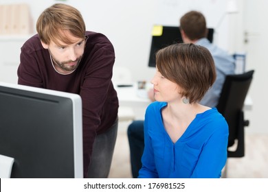 Two colleagues chatting in the office with a handsome bearded young man leaning over an attractive female co-worker