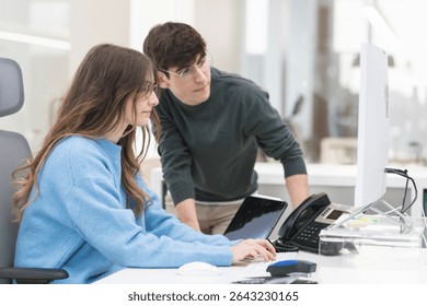 Two colleagues collaborating on a computer project in a bright, modern office, showcasing teamwork and professional support in action