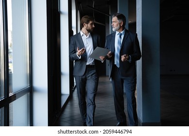 Two colleagues communicating in corridor, partners walking in the modern office - Shutterstock ID 2059446794