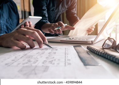 Two colleagues discussing data working and tablet, laptop with on on architectural project at construction site at desk in office - Powered by Shutterstock