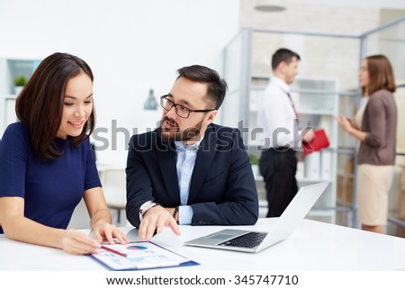 Two colleagues discussing document in working environment in office