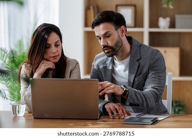 Two colleagues are discussing work while sitting at a desk. A laptop is open in front of them. They appear engaged in conversation. - Powered by Shutterstock - Get 15% off with code: PIKWIZARD15