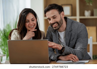 Two colleagues are discussing work while sitting at a desk. A laptop is open in front of them. They appear engaged in conversation. - Powered by Shutterstock - Get 15% off with code: PIKWIZARD15