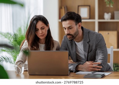 Two colleagues are discussing work while sitting at a desk. A laptop is open in front of them. They appear engaged in conversation. - Powered by Shutterstock - Get 15% off with code: PIKWIZARD15
