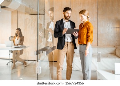 Two Colleagues Dressed Casually Meeting In The Hallway, Solving Some Working Moments With Digital Tablet. Work In Marketing Agency Or Design Studio Concept