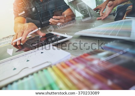 two colleagues interior designer discussing data and digital tablet and computer laptop with sample material and graphics design diagram on wooden desk as concept